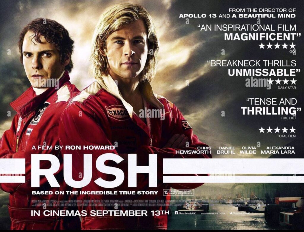 891D09DE-D09A-4BE2-9BAE-3B00F024C9B8 | GotchaMovies Poster for the film Rush: two race car drivers in red suits stand back-to-back with the bold title 'RUSH' in front of a dramatic sky and race imagery behind them.