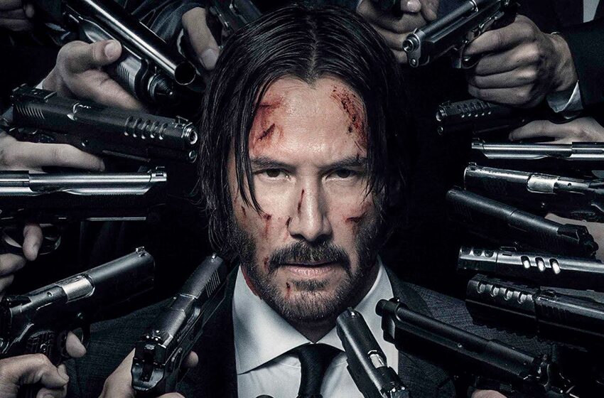 image | GotchaMovies Man in a suit with facial cuts, surrounded by numerous guns pointed at him.