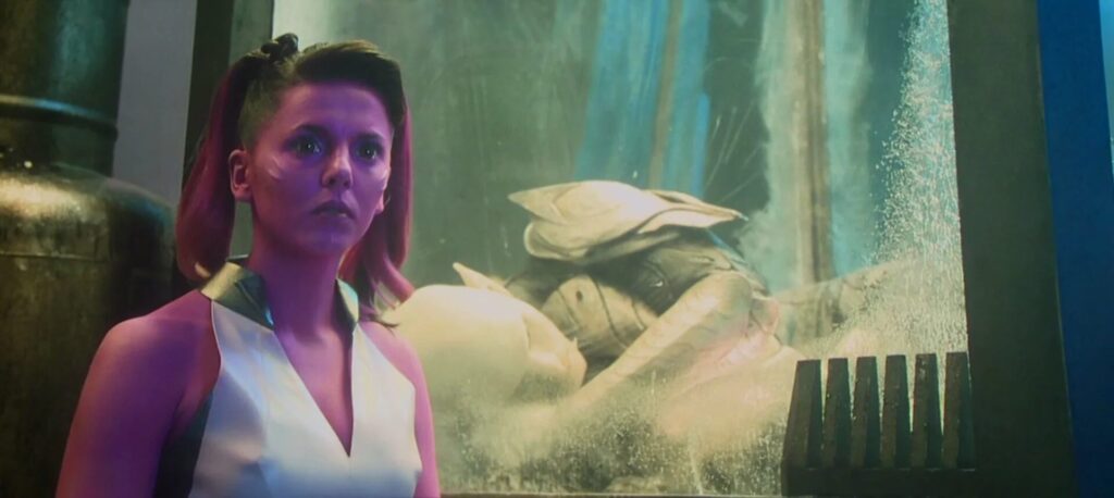 Woman with pink hair in a white and pink futuristic outfit stands in a neon-lit lab, looking off to the side.