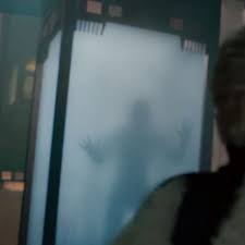 Two hands pressed against a frosted glass pane, with a blurry silhouette of a person behind it.