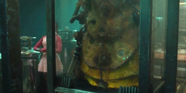 Large animal inside a glass tank with scuba gear and a person in pink in the background.