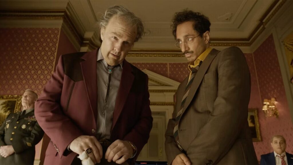 image | GotchaMovies Two men in vintage suits lean over a table in a luxuriously decorated room, with other figures in the background.