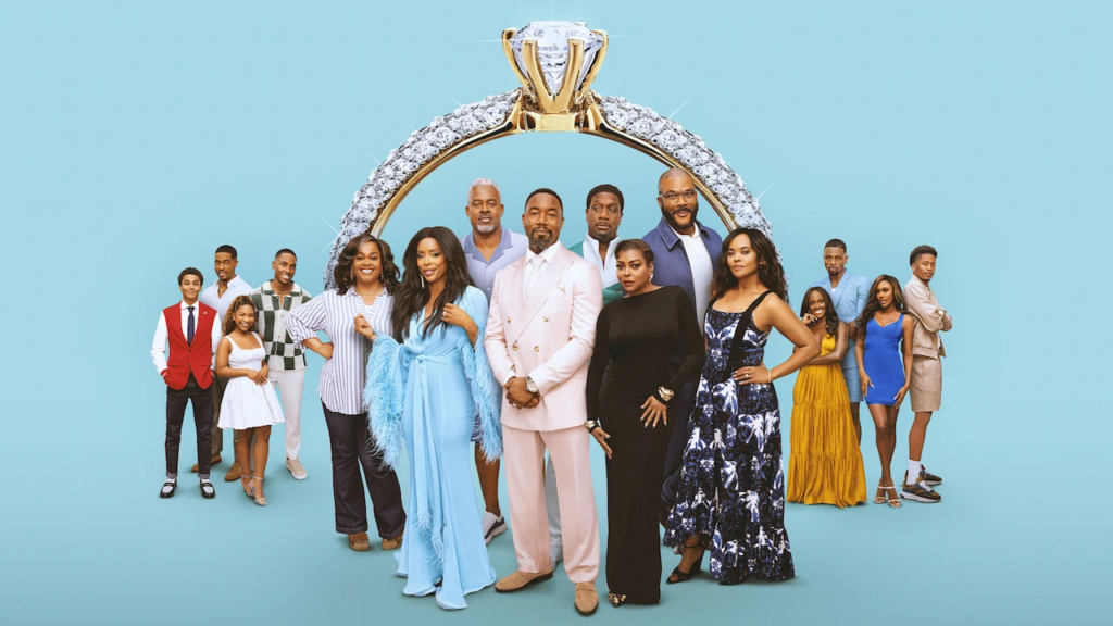Diverse group of people posing in front of a large diamond engagement ring prop on a blue backdrop.