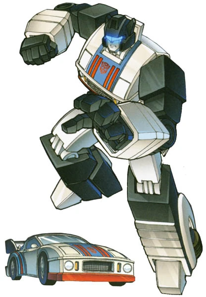 image | GotchaMovies A large transforming robot standing over a blue race car, ready to spring into action, with Autobot insignia on its chest.